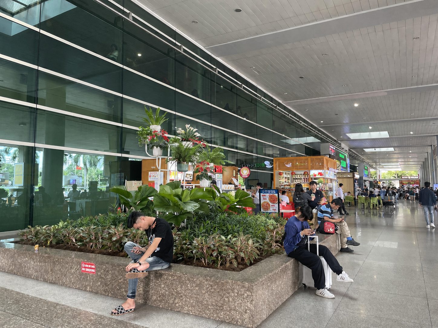 タンソンニャット空港のターミナル、植え込みのふちに座ってスマホを見ている人たち